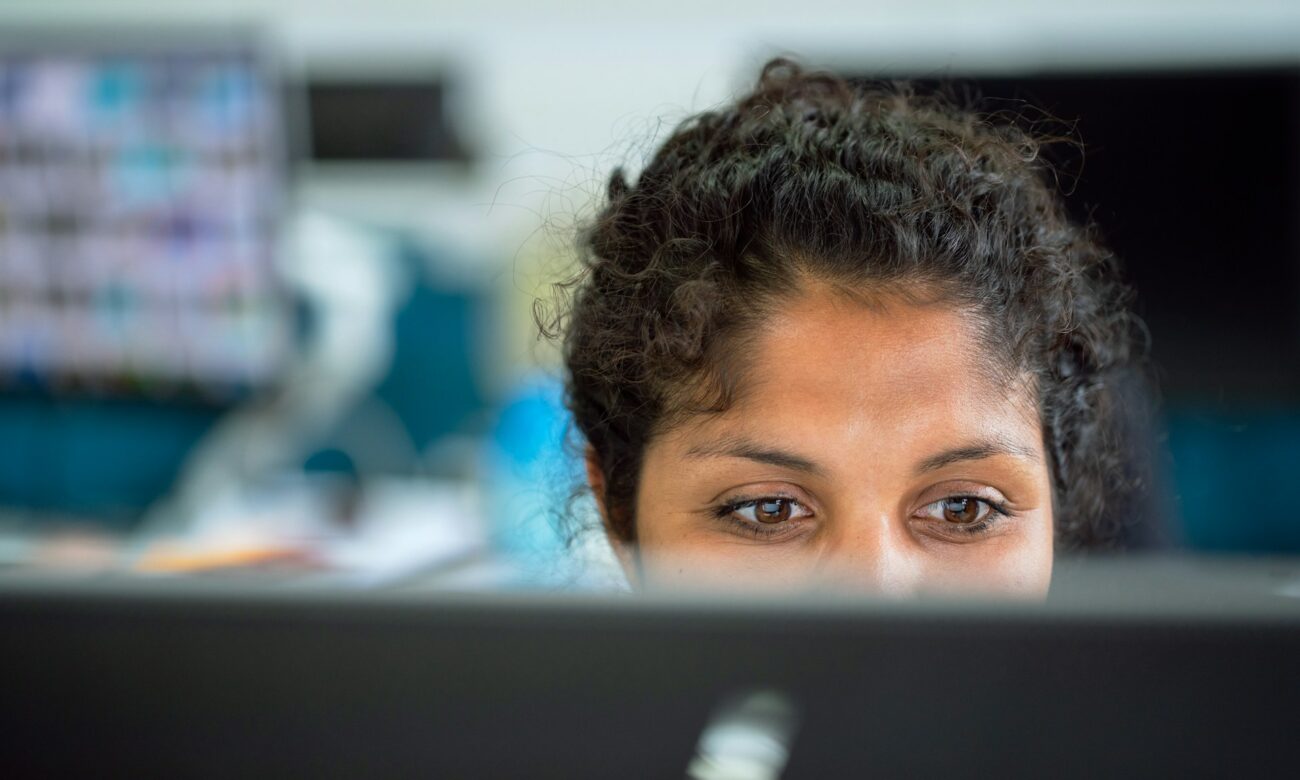 The top of a person's head is seen behind their monitor. They're looking at the monitor, not at the camera.